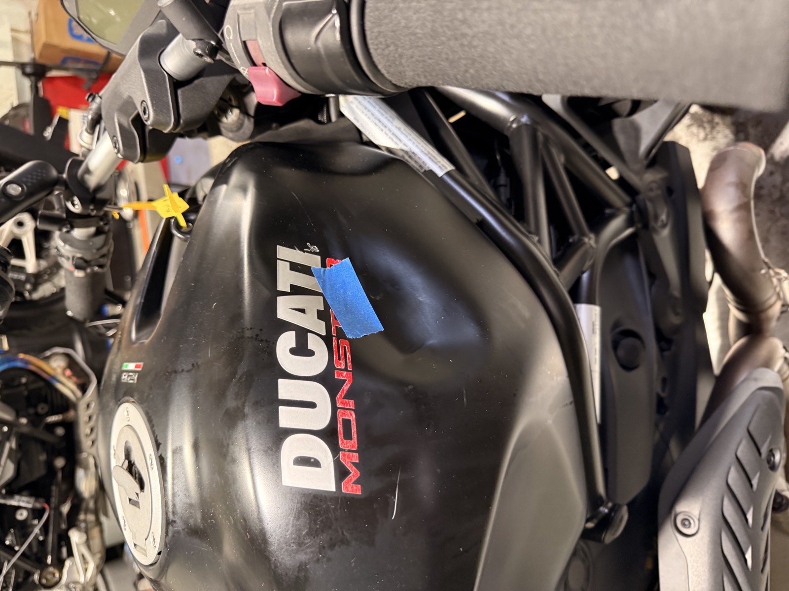 The fuel tank of a 2015 Ducati Monster 821 Dark on a shop stand, with blue tape marking damaged areas